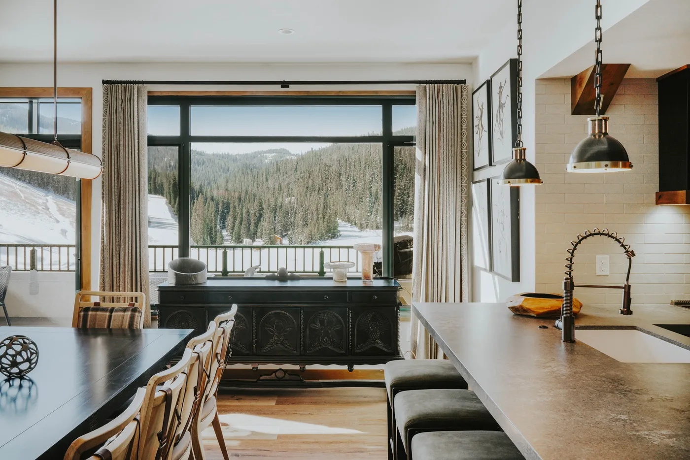 A dining area and kitchen overlook a wooded, snow-covered landscape through large windows.
