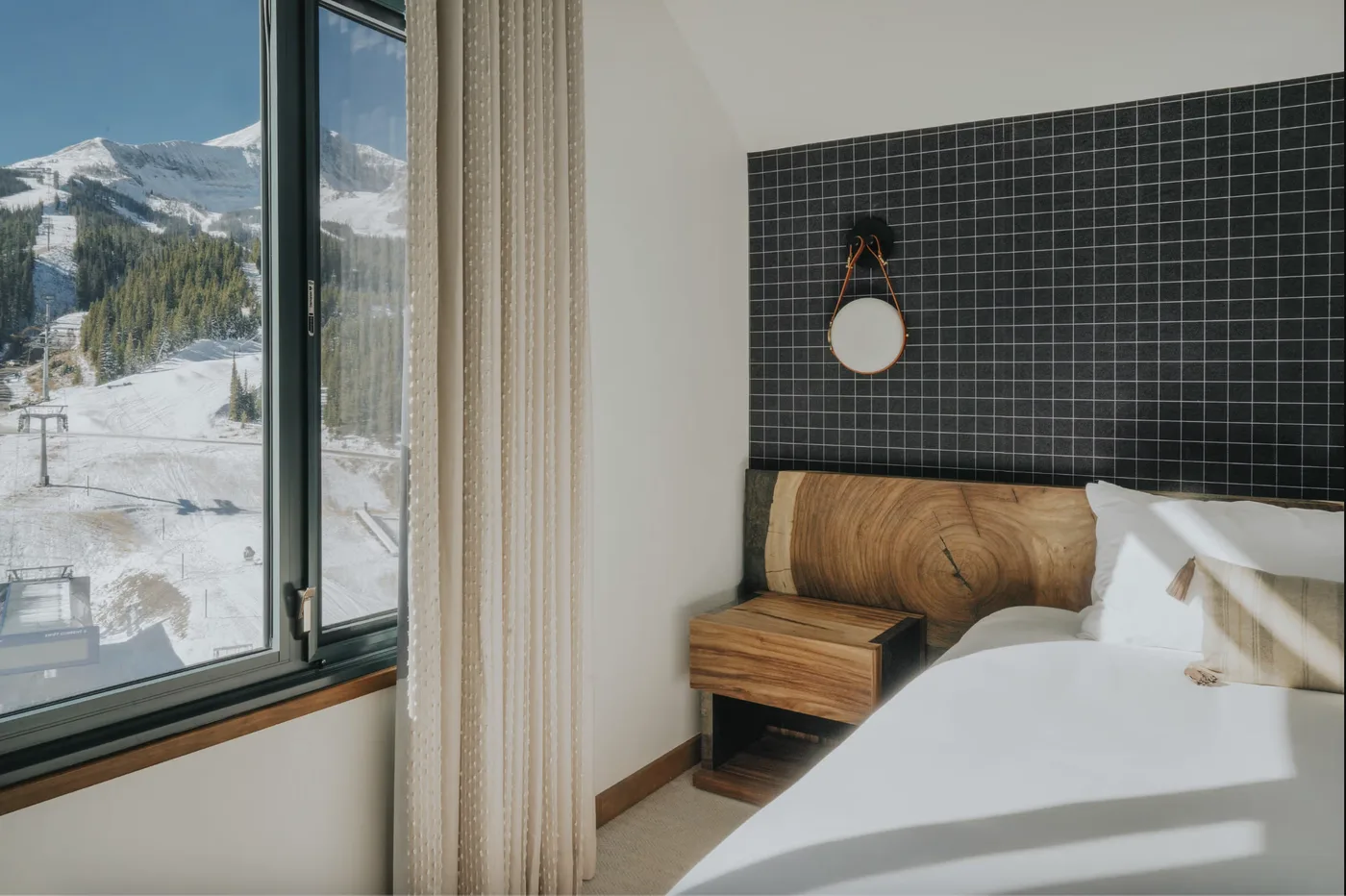 A bedroom with a bed beside a large window overlooking a snowy mountain landscape.