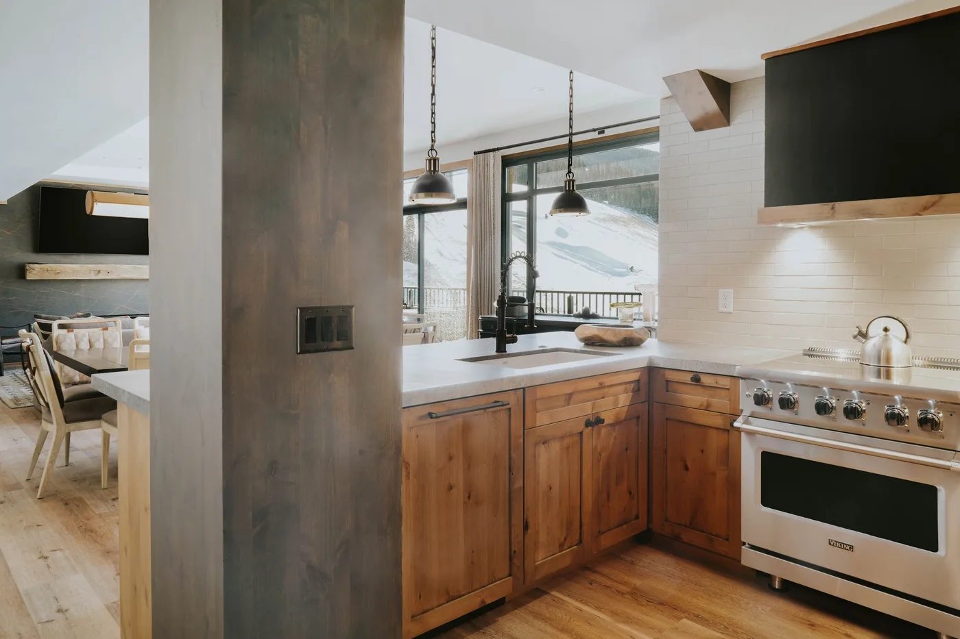 A bright kitchen with wooden cabinets, a central island, and windows overlooking a snowy landscape.