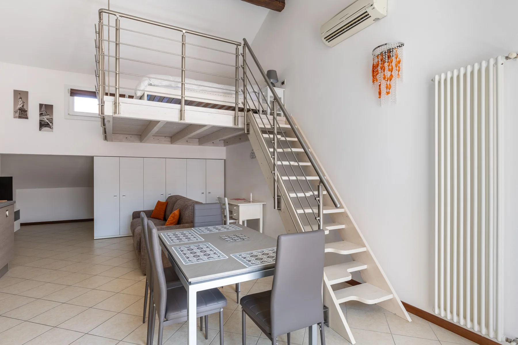 A loft-style living and dining area with a staircase leading to an upper sleeping space.