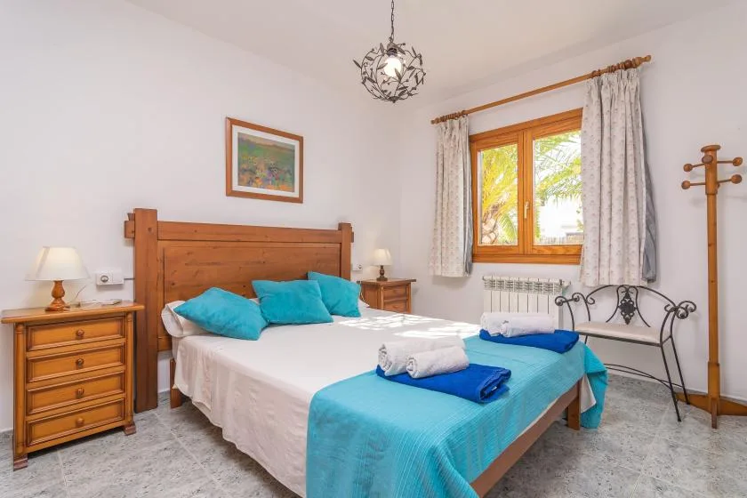 A bedroom with a wooden bed, turquoise bedding, and a window with curtains.