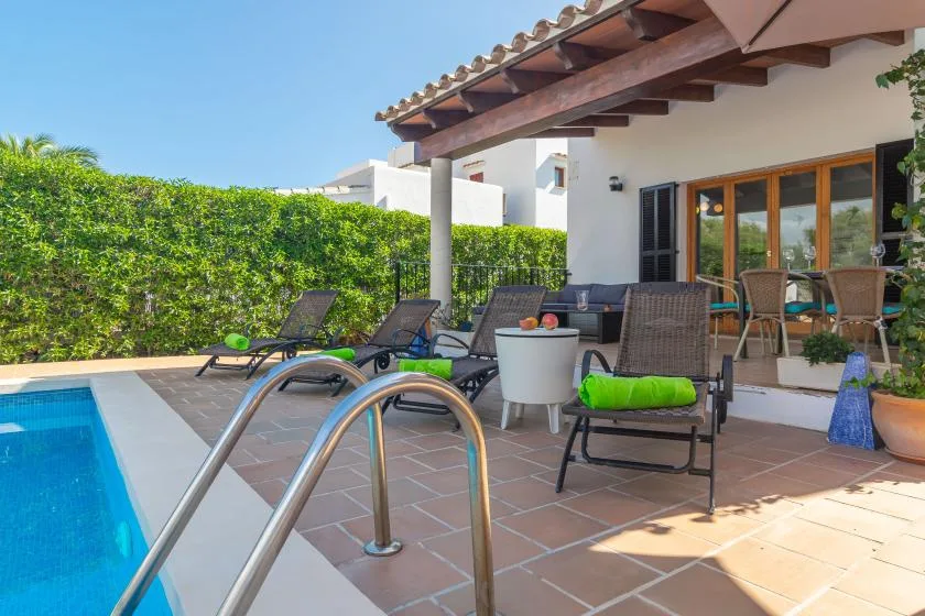 A poolside patio with outdoor seating and a hedge along the edge.