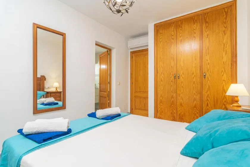 A bedroom with white bedding, turquoise pillows, and wooden wardrobes.