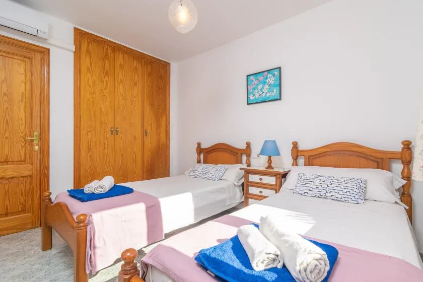 A bedroom with two beds, wooden wardrobes, and folded towels on the bedding.