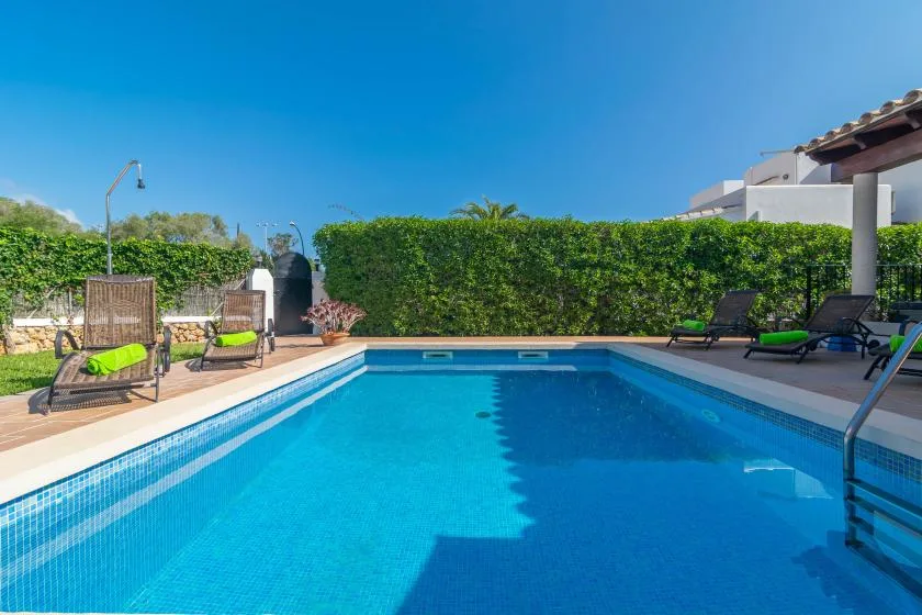 An outdoor swimming pool is surrounded by a paved deck and greenery.