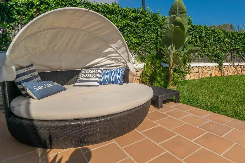 An outdoor patio with a round cushioned daybed beside a green lawn.