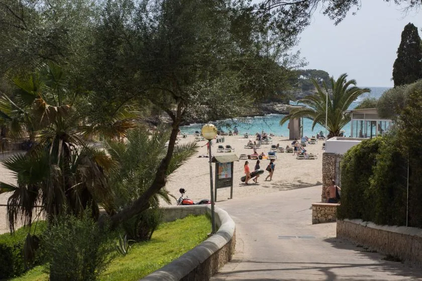 A landscaped path leads toward a sunny beach with people and turquoise water.