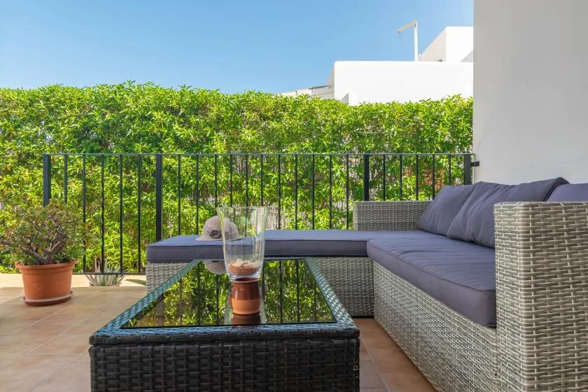 An outdoor patio seating area with a glass-topped table beside a hedge.
