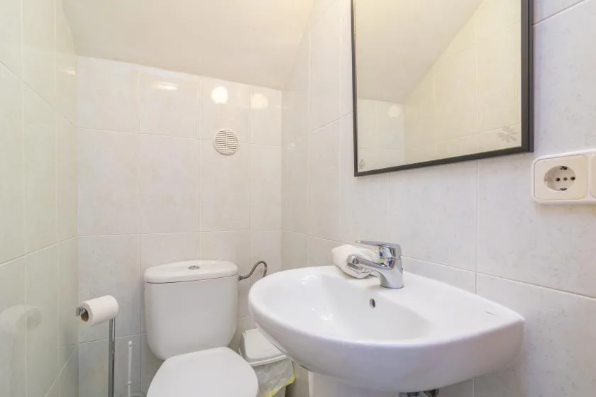 A tiled bathroom with a toilet and a wall-mounted sink.