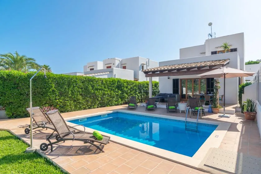 A swimming pool sits beside a patio with lounge seating and a white building.