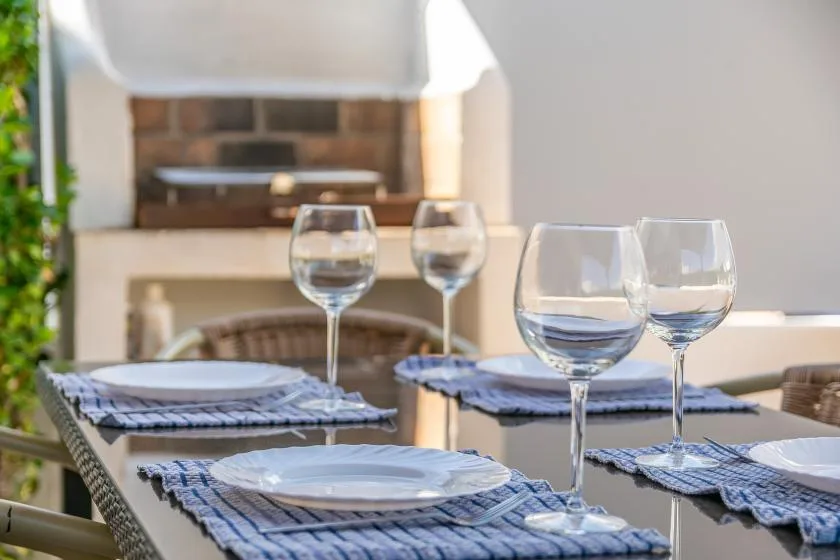 An outdoor dining table is set with plates, woven placemats, and wine glasses.