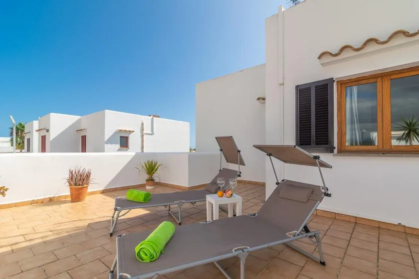 A sunny tiled patio with reclining loungers, a small table, and potted plants.