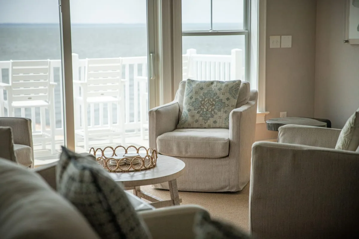 A bright living room with cushioned seating and a view through large windows.
