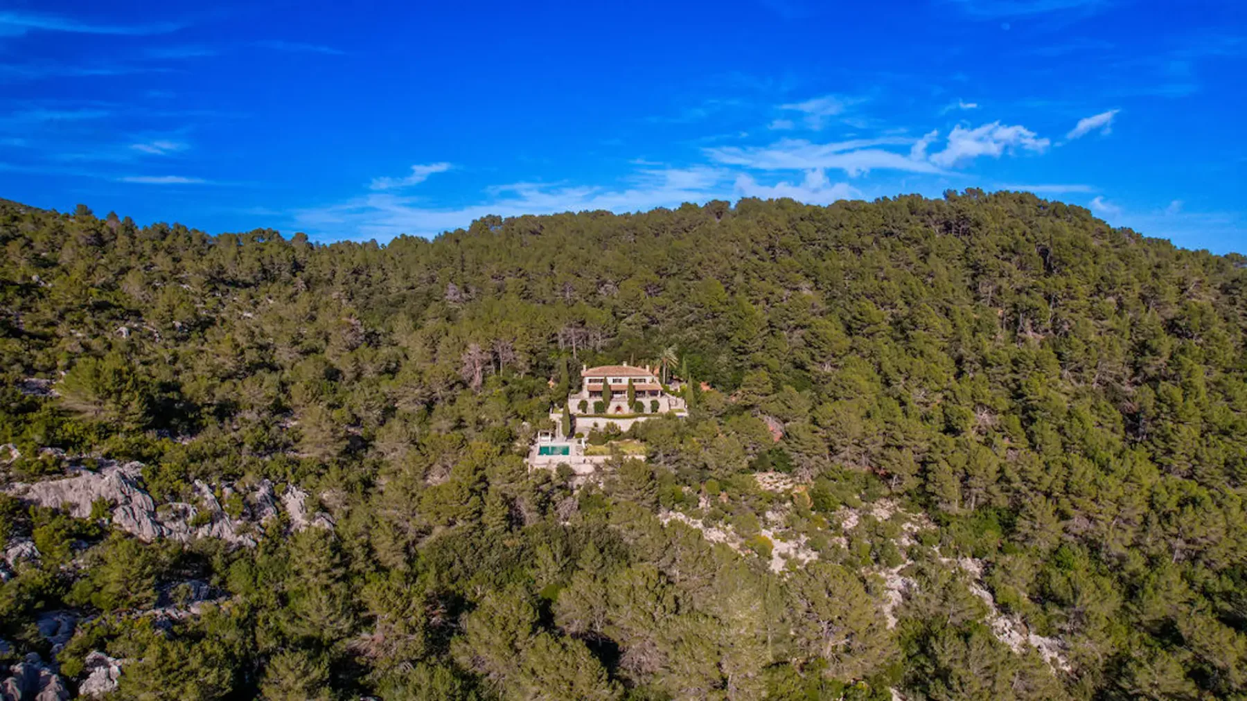 Aerial view of a house surrounded by wooded hills.