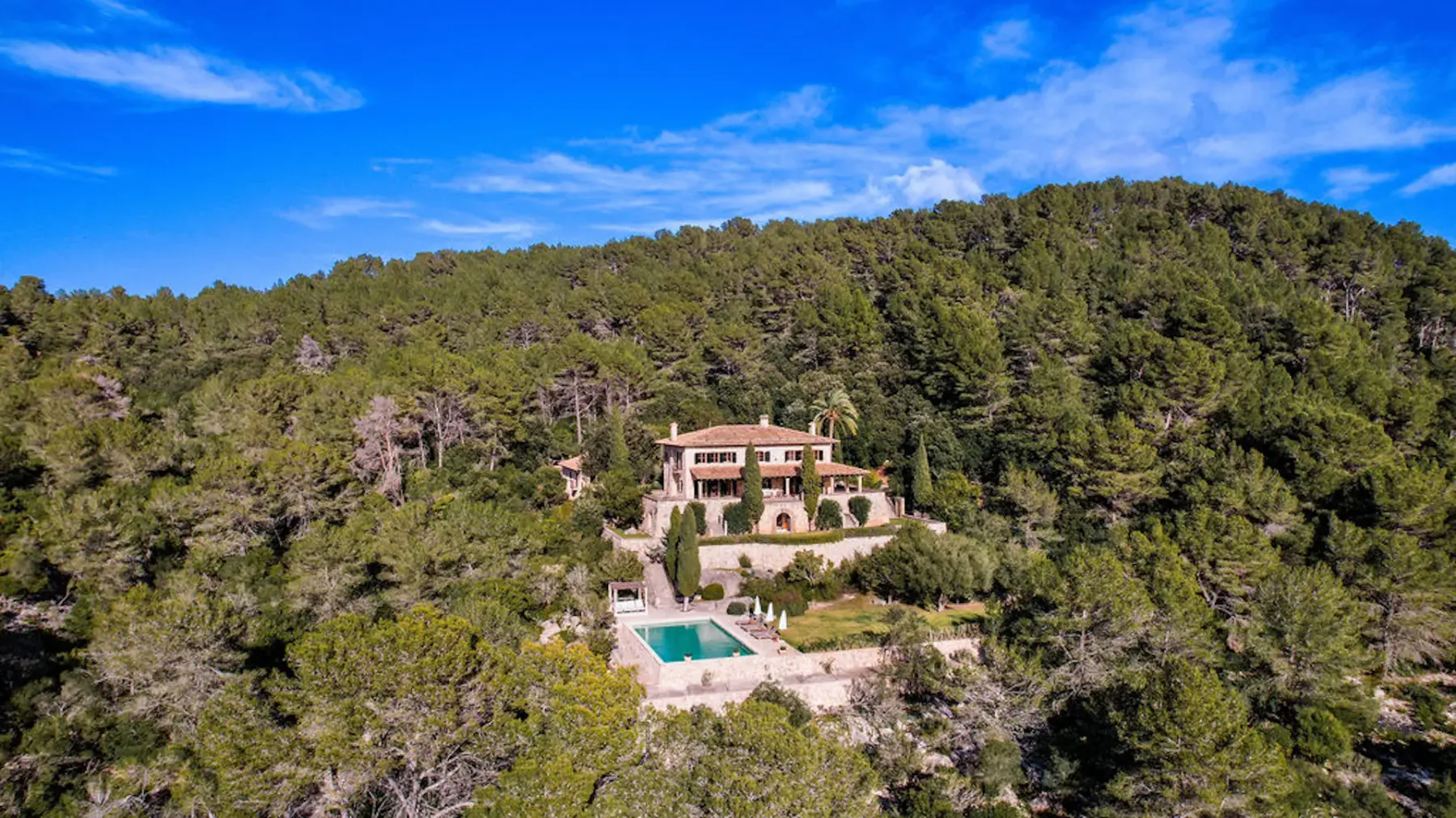 Aerial view of a house and pool surrounded by a wooded hillside.