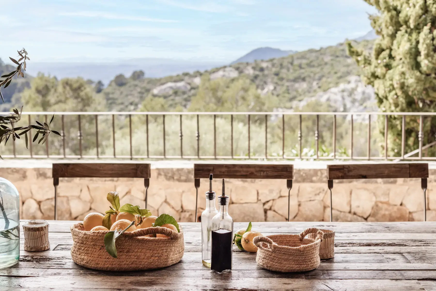 A terrace dining table with baskets and bottles overlooks a green hillside.
