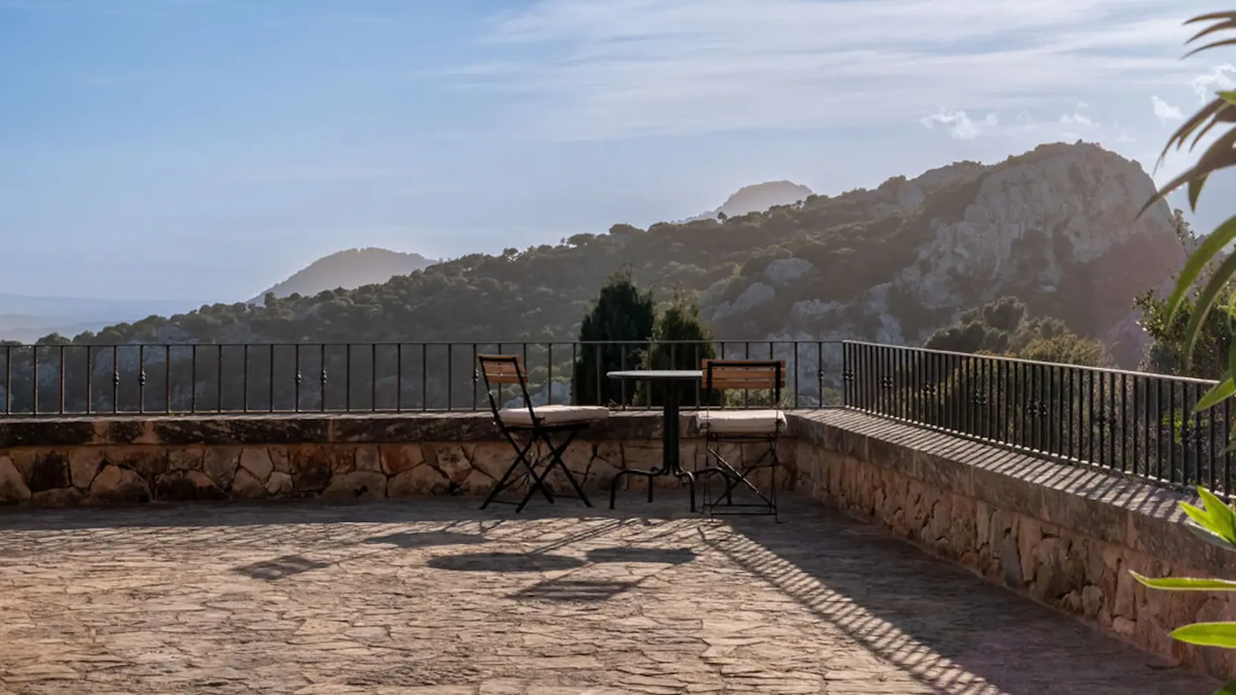 A stone terrace with outdoor seating overlooks a mountain landscape.