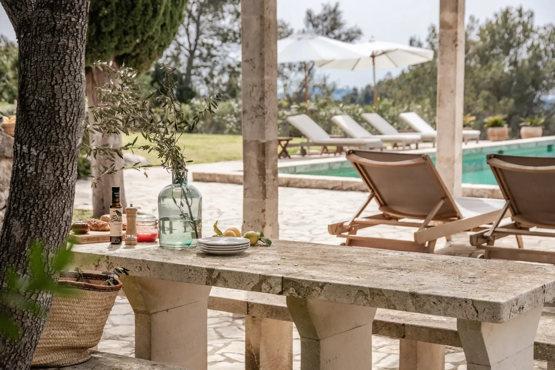 A stone outdoor dining table sits beside a swimming pool.