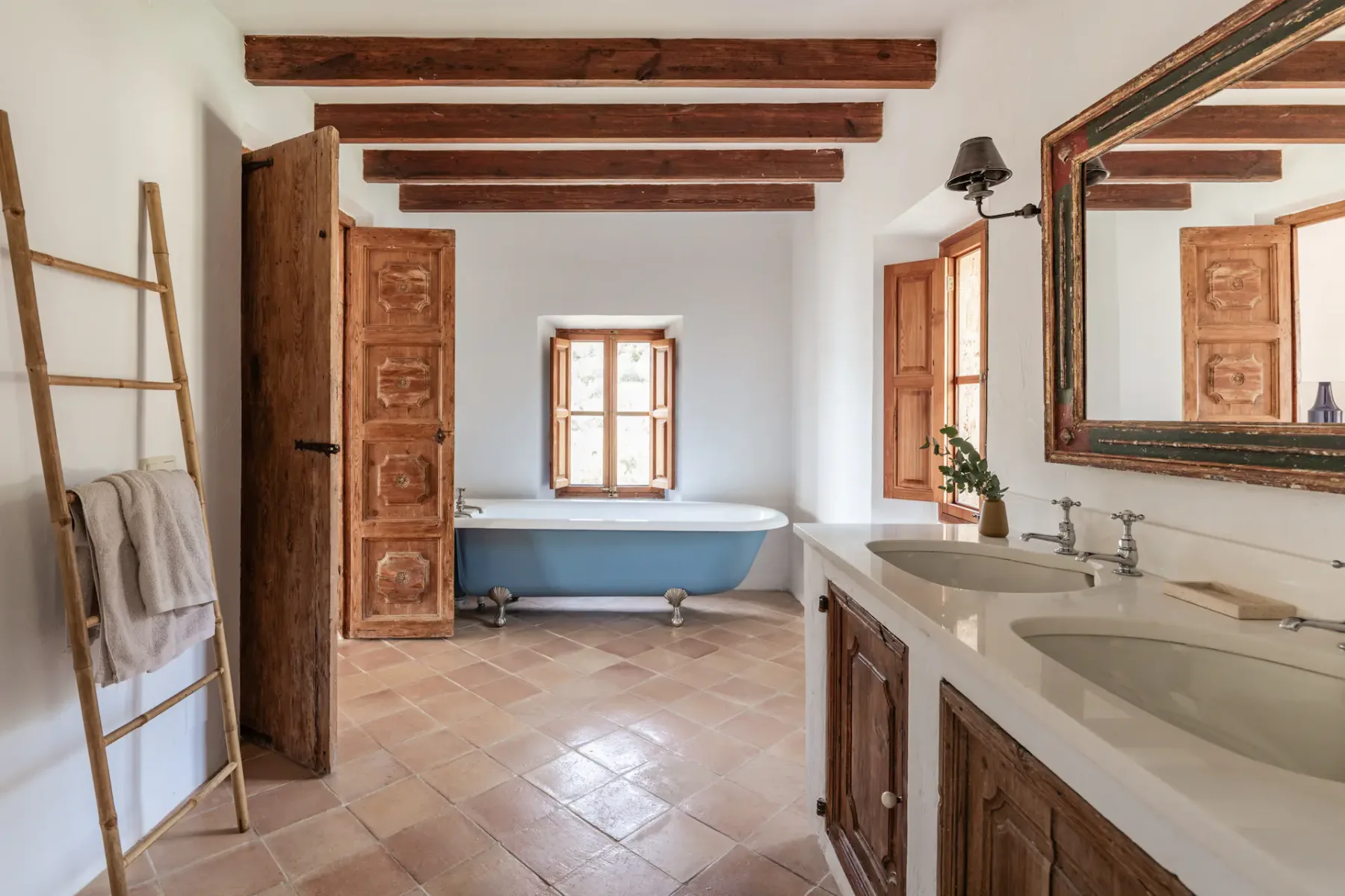 A bathroom with a freestanding tub, double sinks, and exposed ceiling beams.