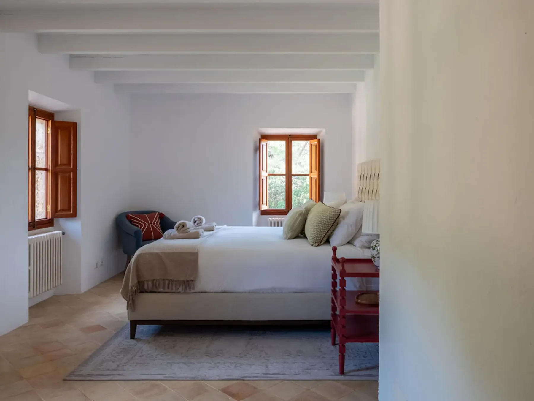 A bedroom with a neatly made bed, wooden windows, and exposed ceiling beams.