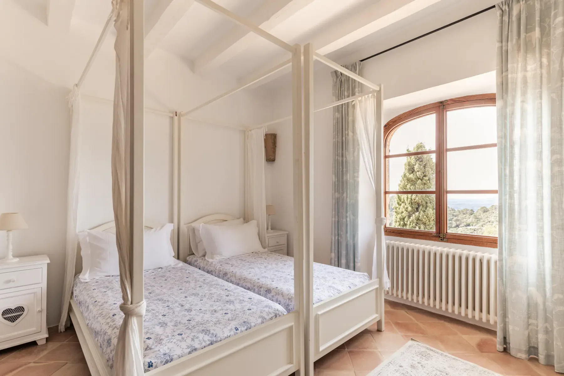 A bright bedroom with two beds beneath a large arched window.