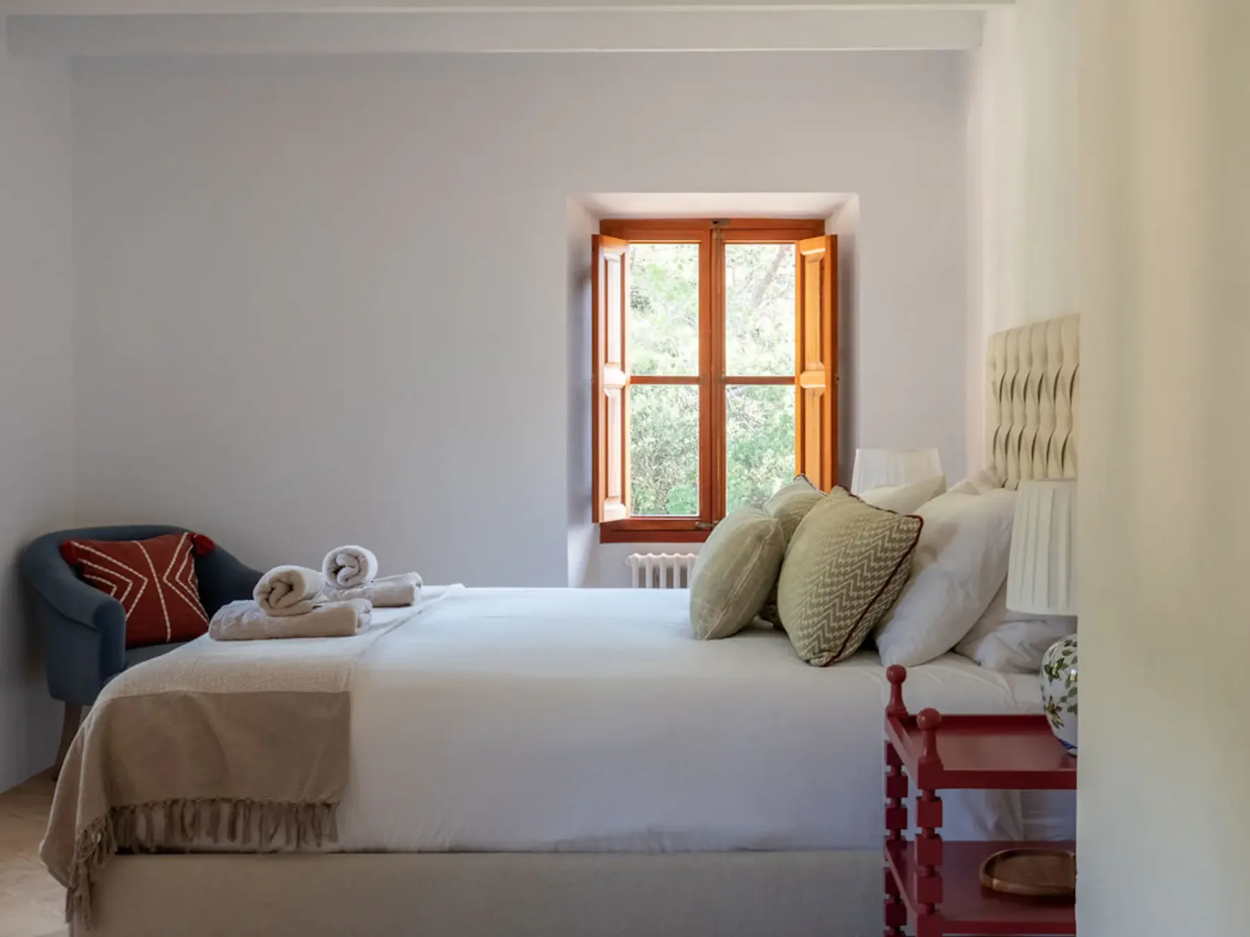 A bright bedroom with a neatly made bed beside an open window.