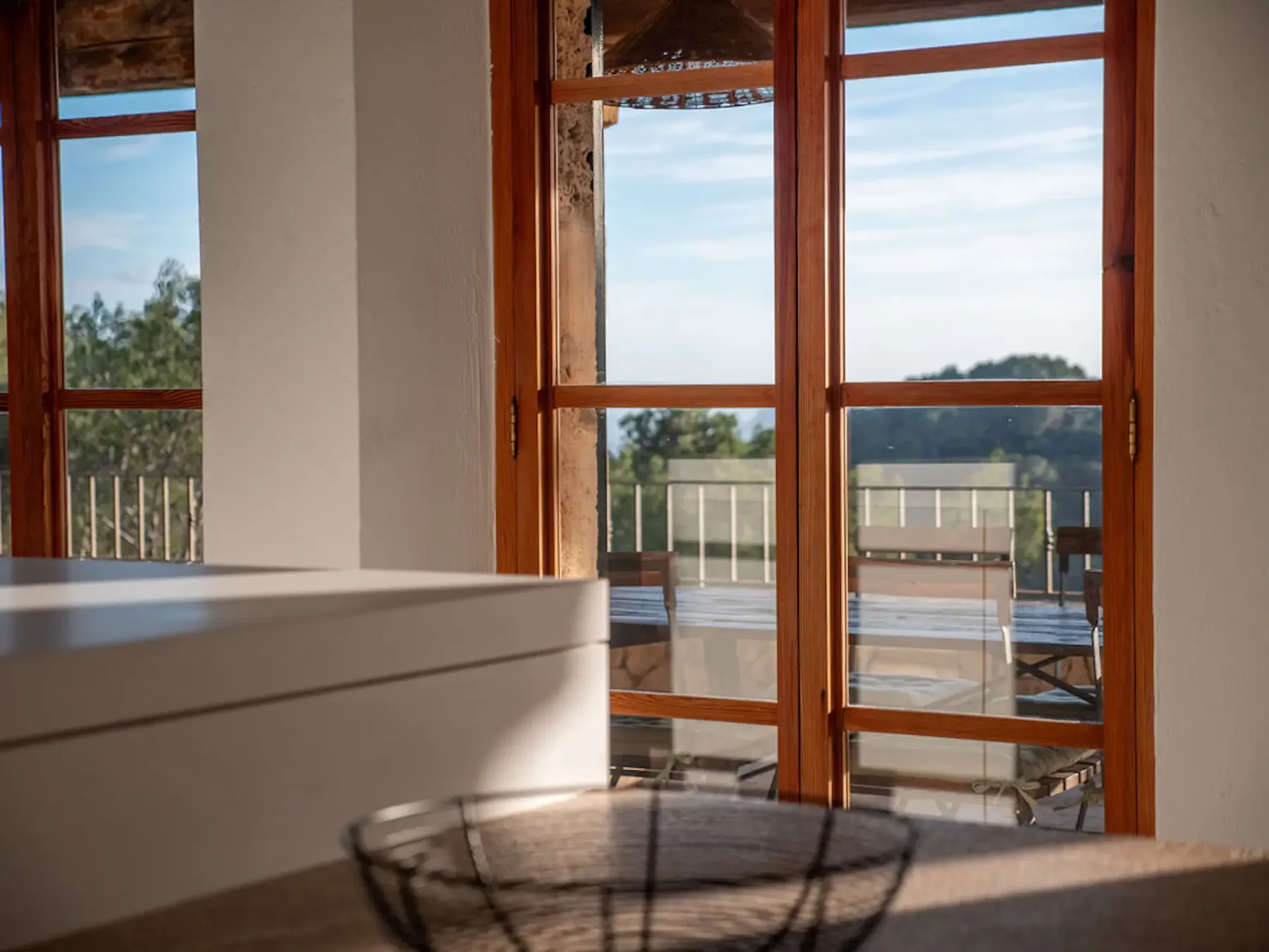 A bright interior opens onto a terrace through large wooden-framed windows.