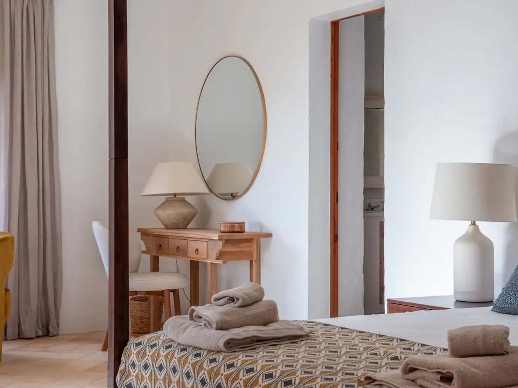 A bedroom with a neatly made bed and a wooden dressing table.