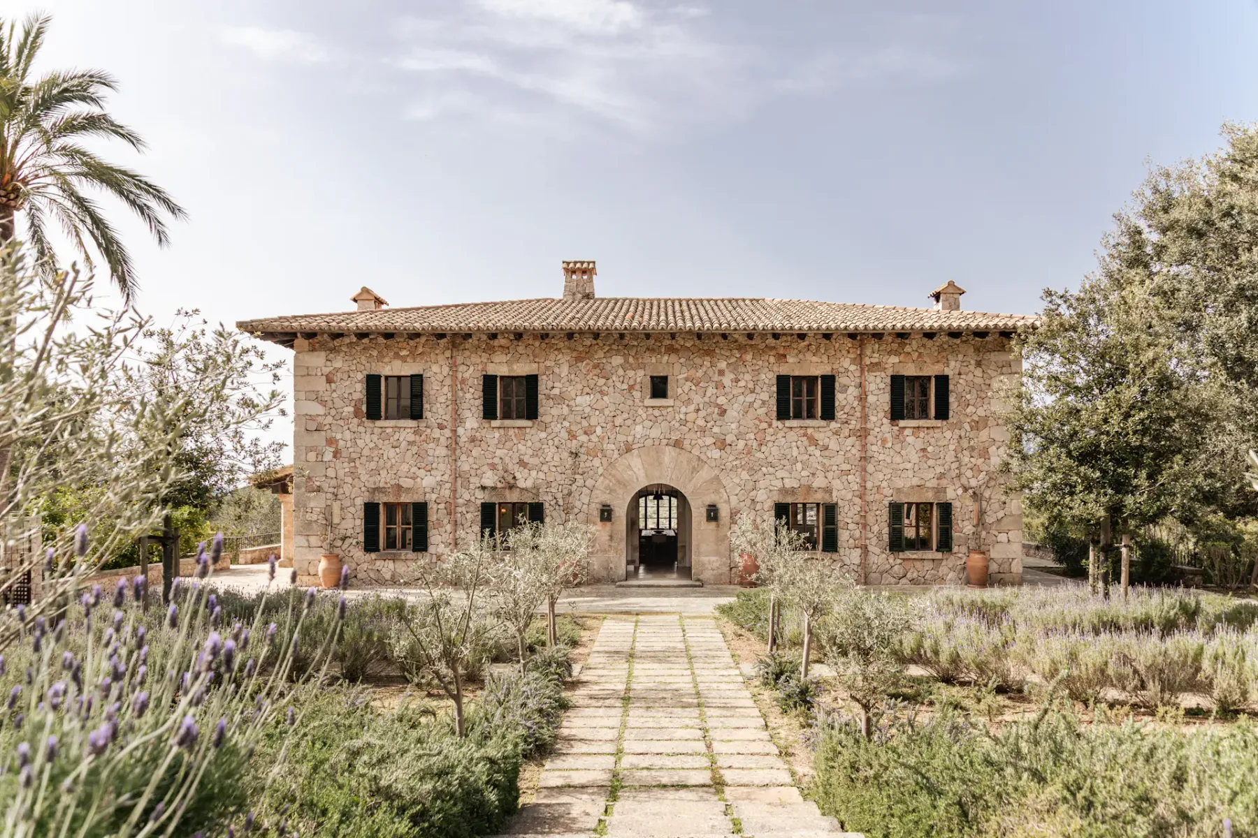 A stone house facade faces a garden path bordered by flowering plants.
