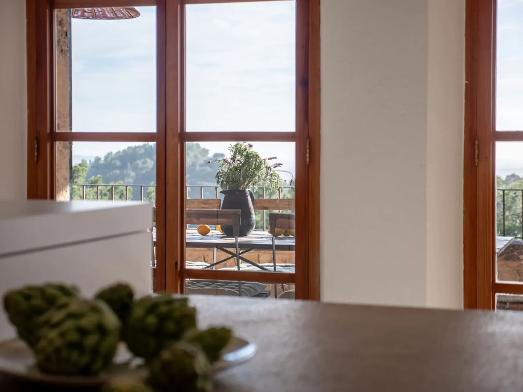 A dining area looks through tall windows onto a terrace with seating and greenery.
