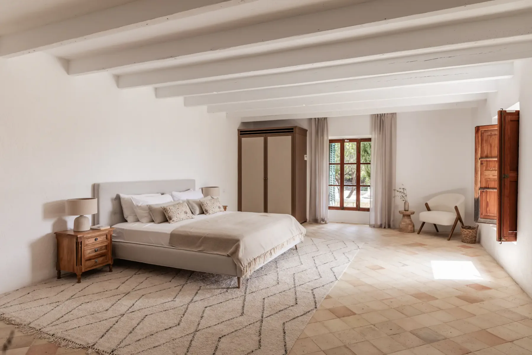 A bright bedroom with a large bed and exposed ceiling beams.