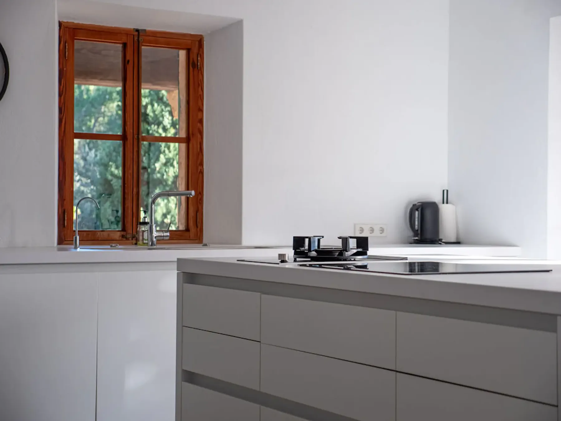 A bright kitchen with a cooktop and a wooden-framed window.