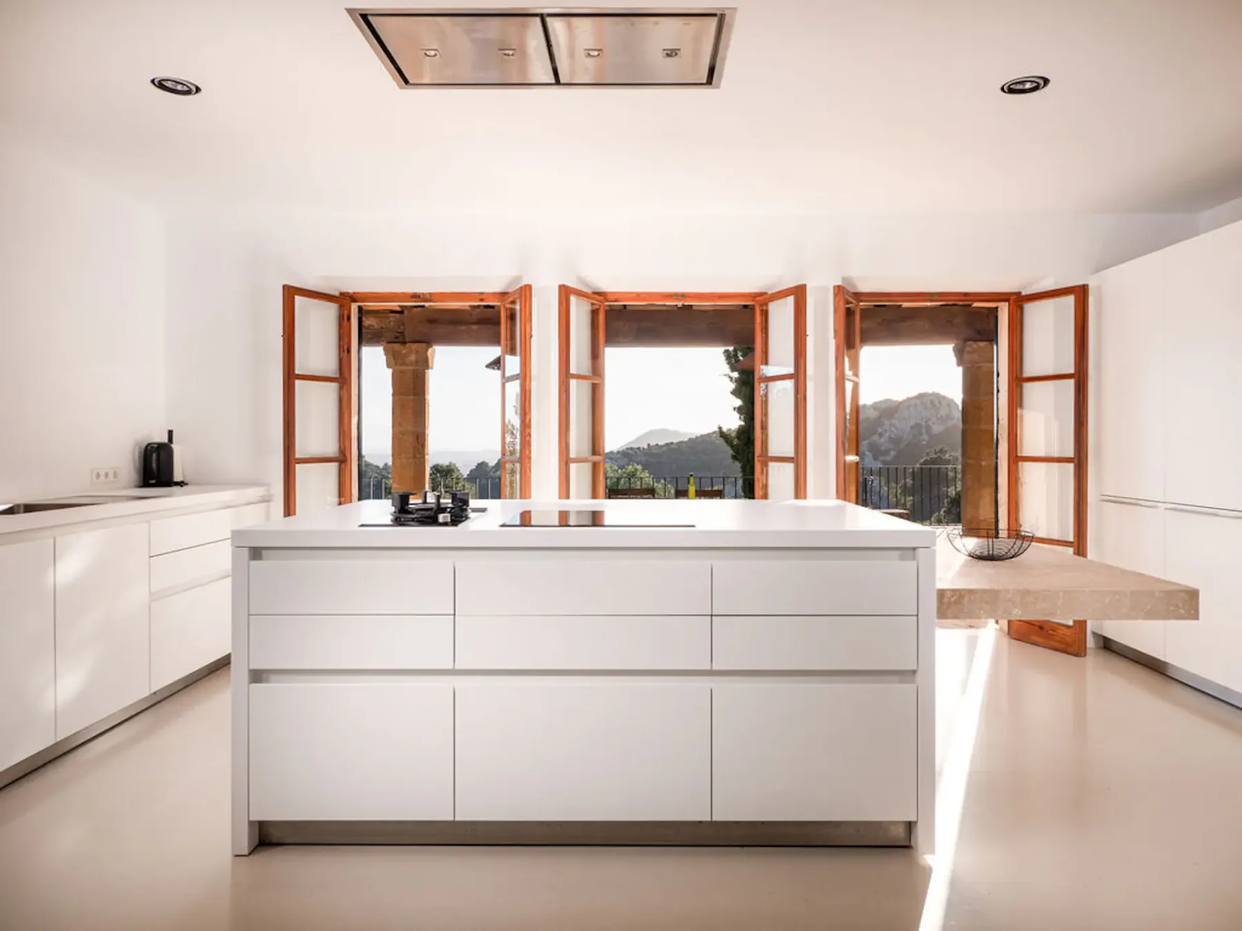 A bright kitchen with a central island and open wooden-framed windows.