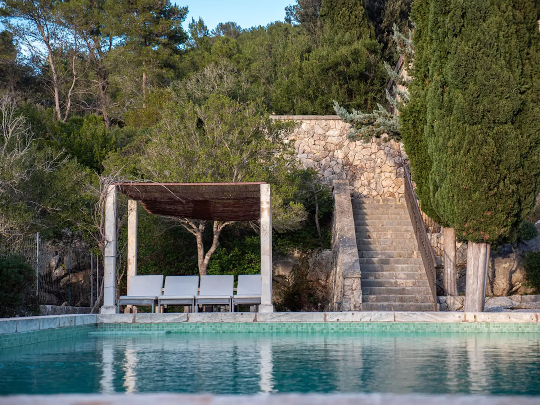 A swimming pool sits beside stone steps and a shaded seating area.
