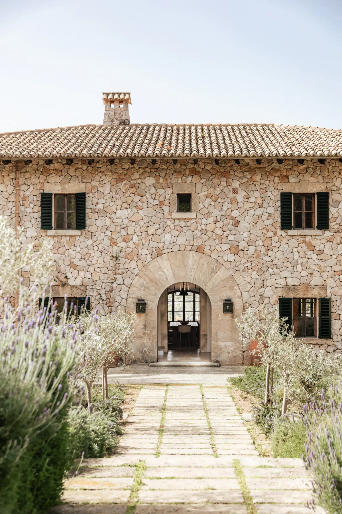 A stone house facade with a tiled roof and a path leading to the arched entrance.