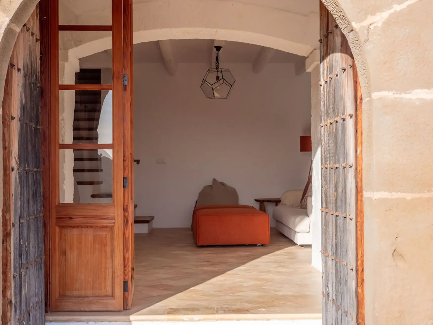 An arched wooden doorway opens onto a bright room with seating.