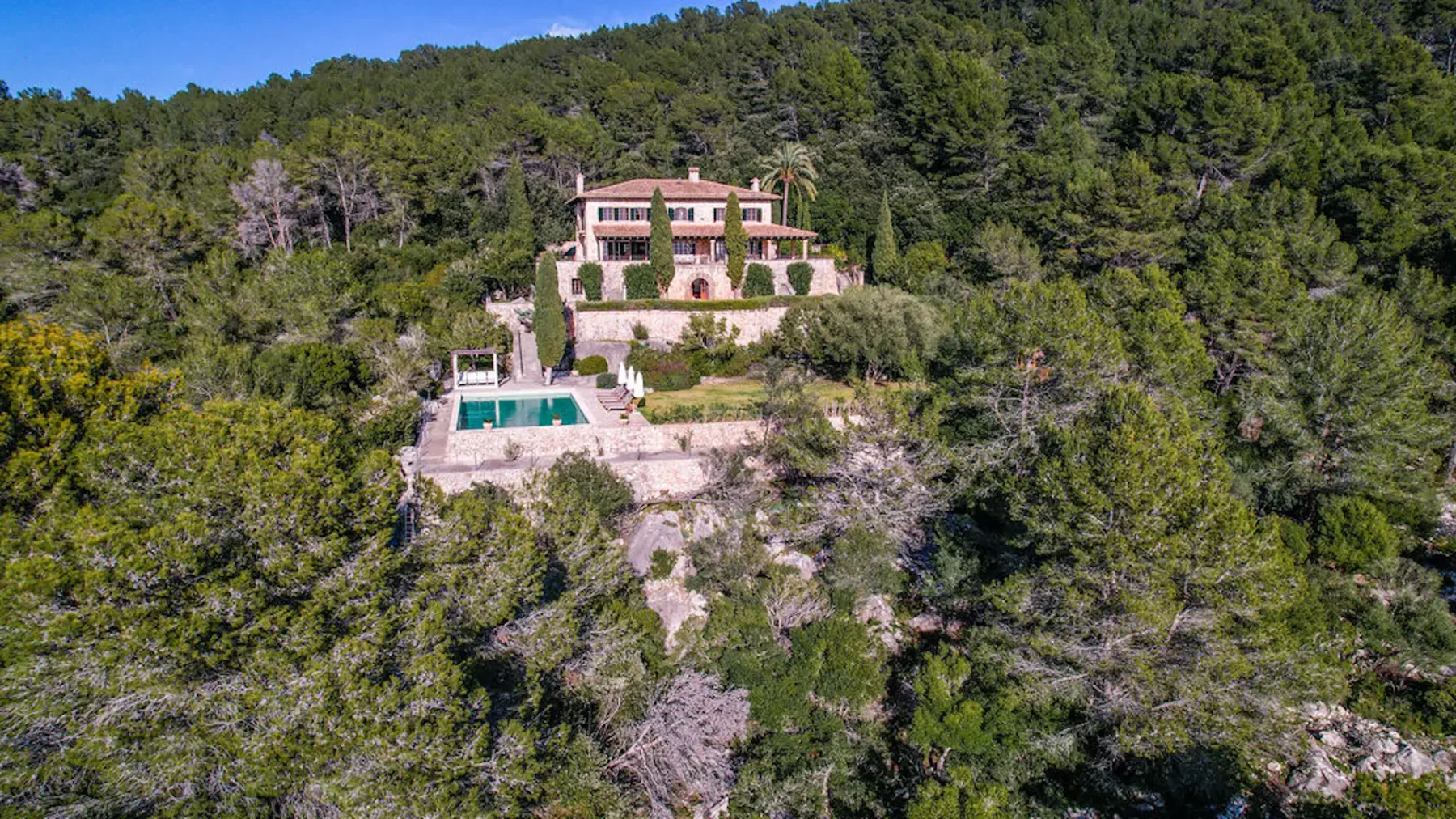 A house and swimming pool sit on a hillside surrounded by dense woodland.