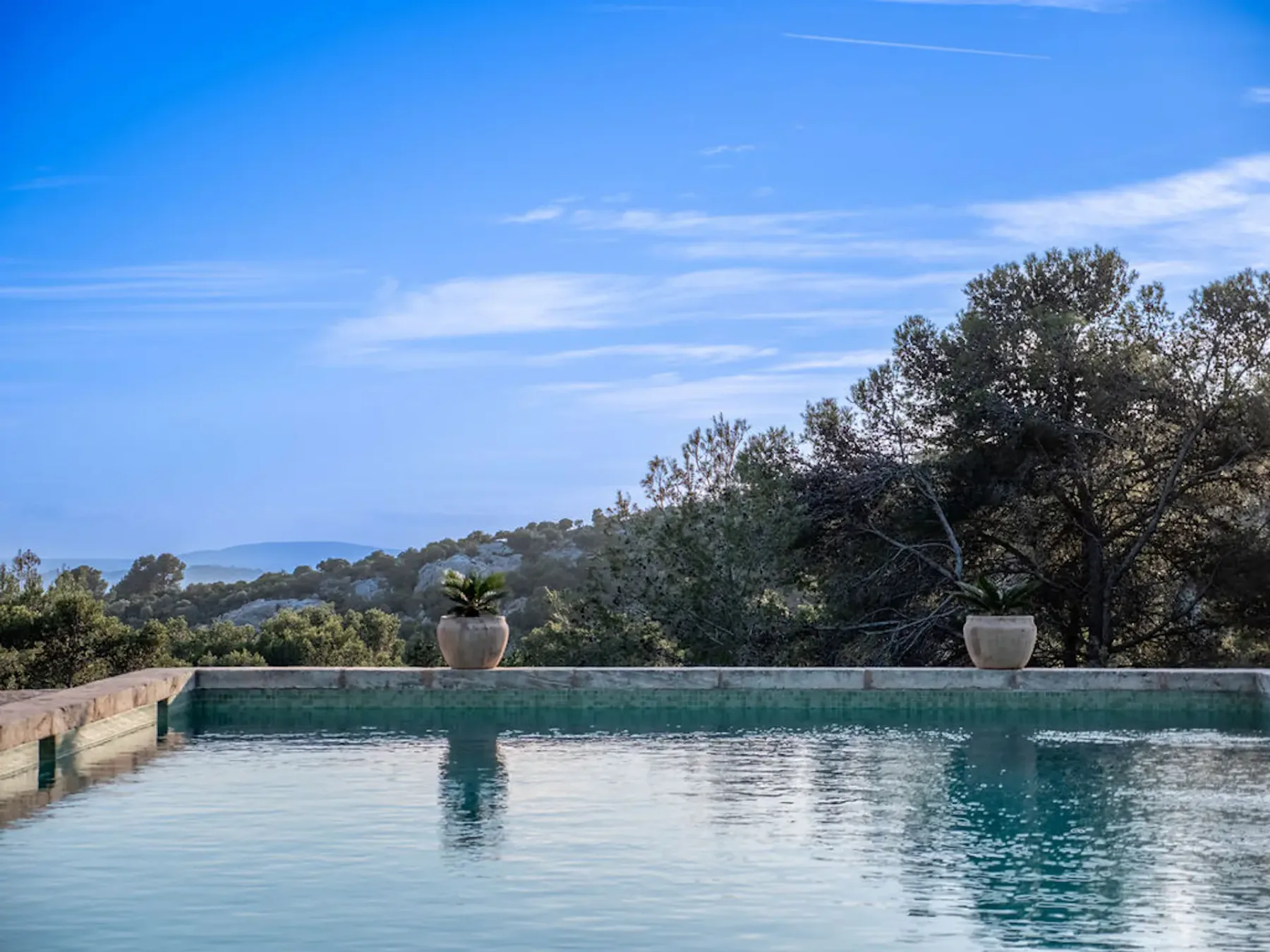 A swimming pool overlooks tree-covered hills beneath a blue sky.