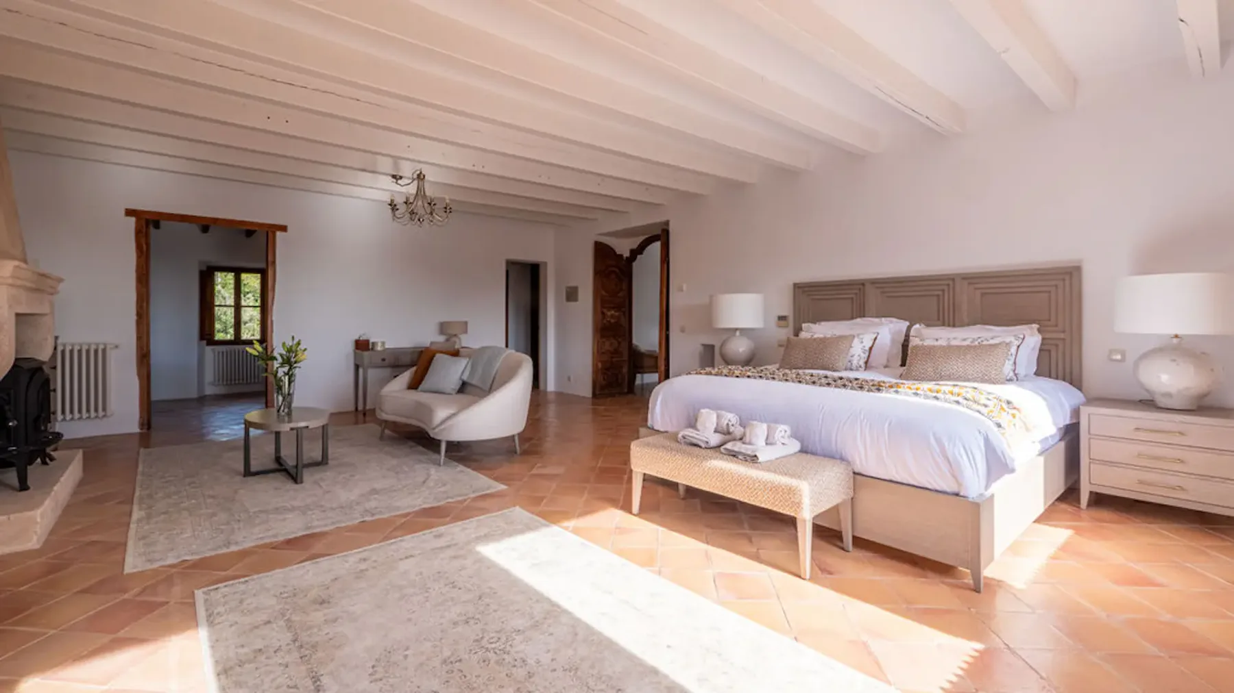 A bedroom with a large bed, seating area, and exposed ceiling beams.