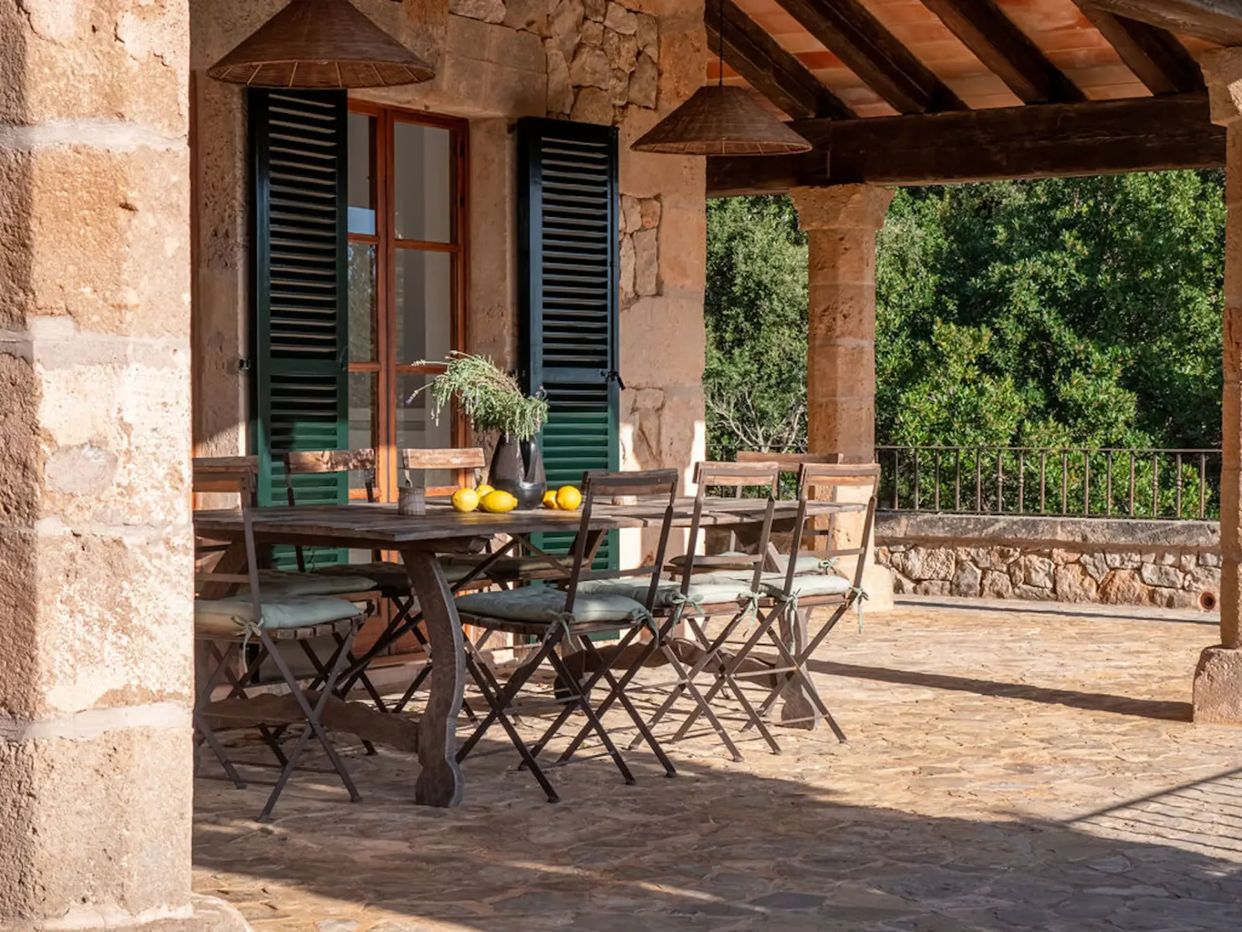 An outdoor dining area with a wooden table and folding chairs beneath a covered terrace.
