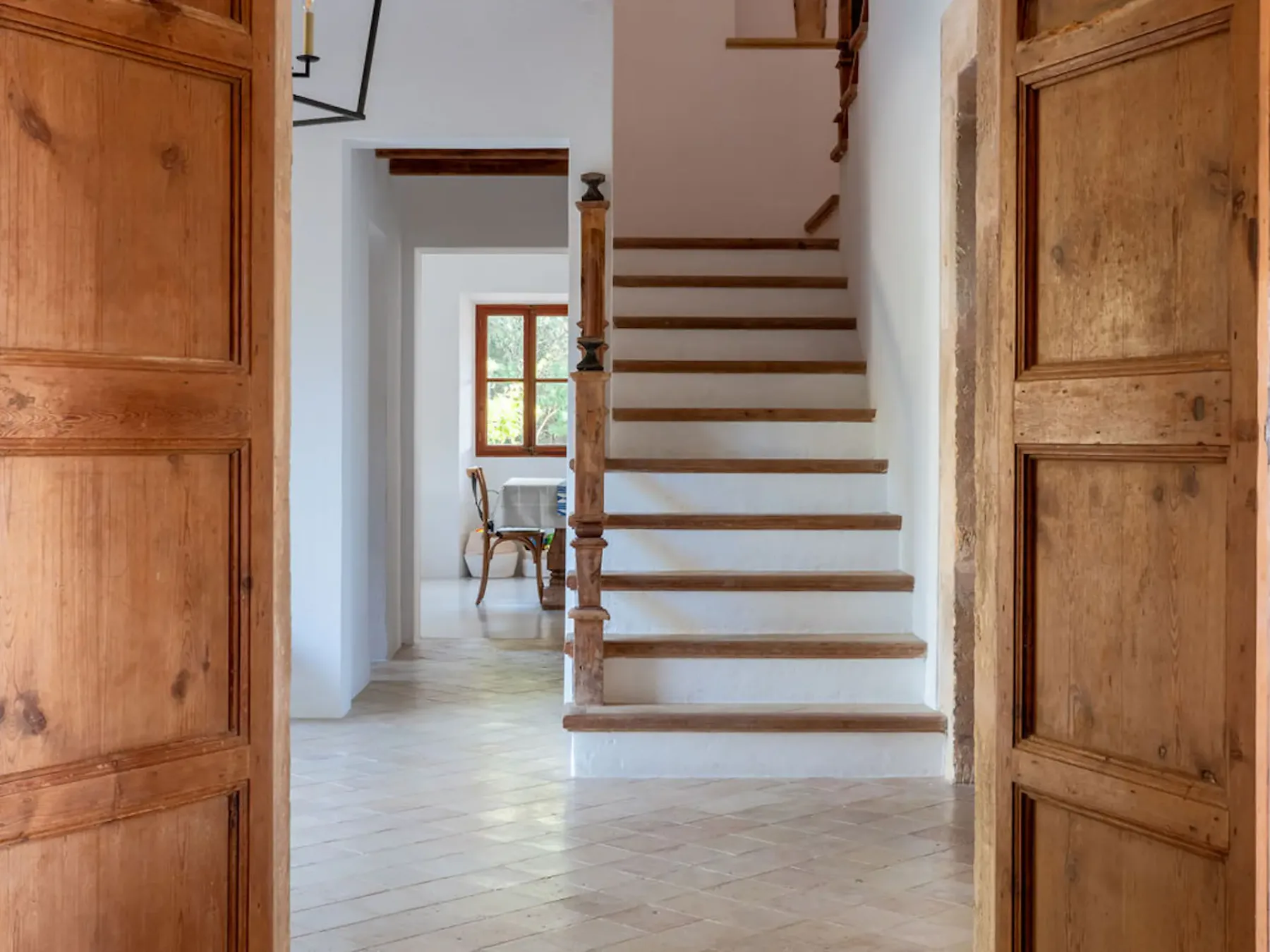 A wooden staircase rises through a bright interior hallway.