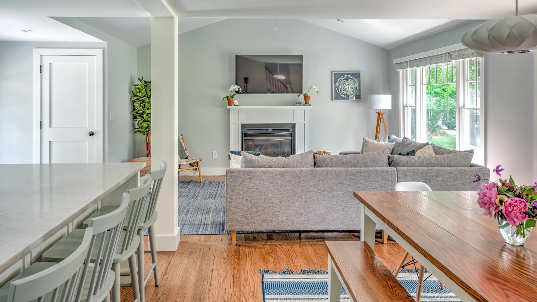 A bright living room with seating around a fireplace and large windows.
