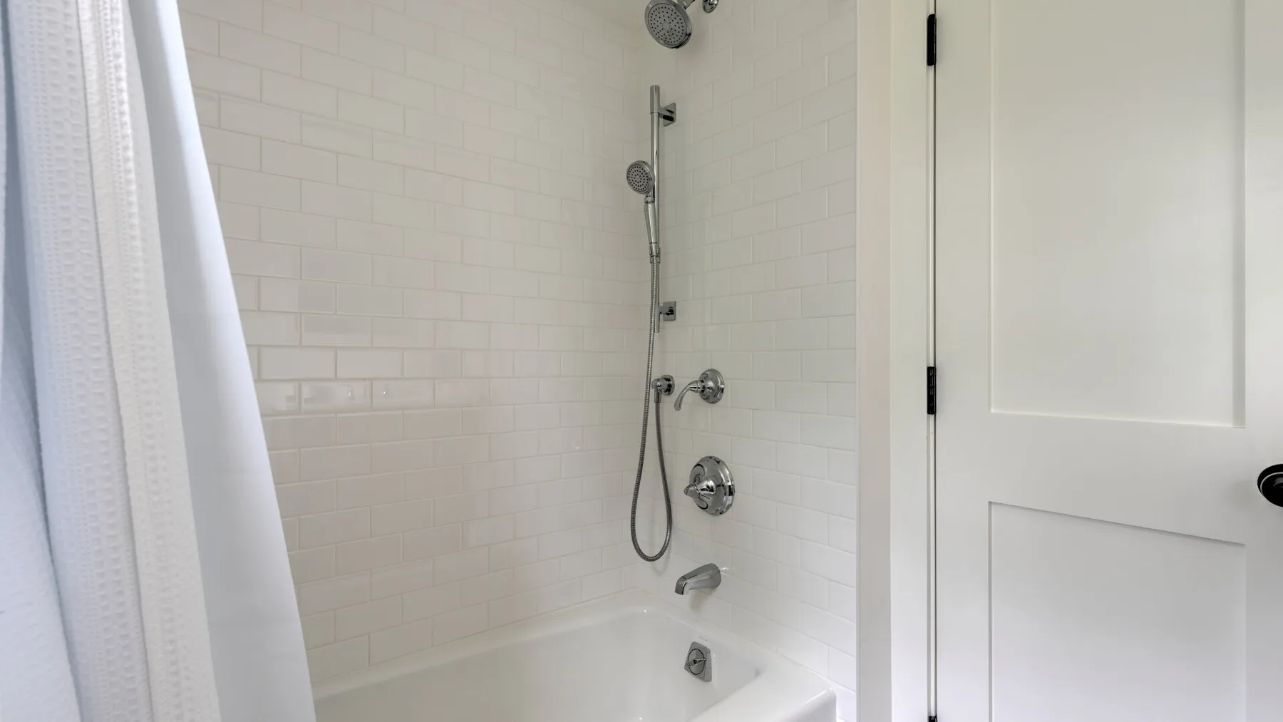A tiled bathroom shower with a handheld showerhead and white curtain.