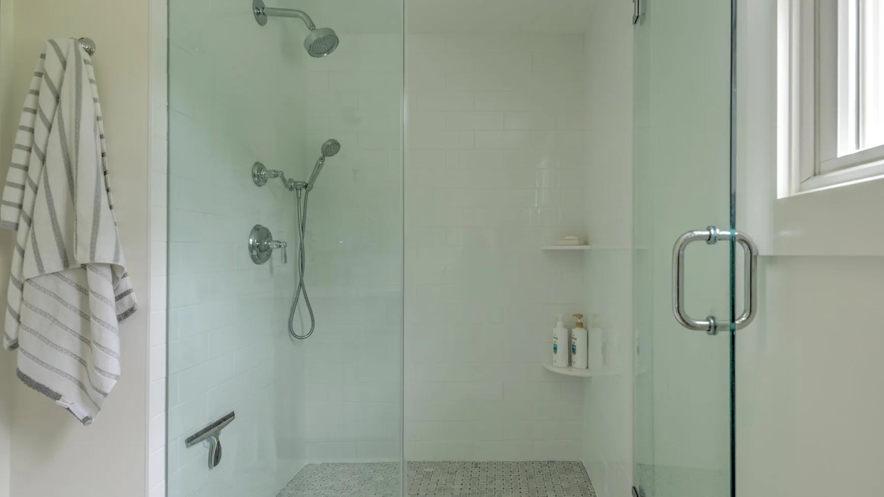 A tiled bathroom shower with glass panels and a towel hanging nearby.