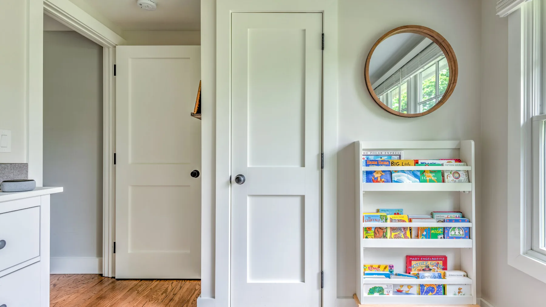A bright room with a white door, round mirror, and shelves of books.