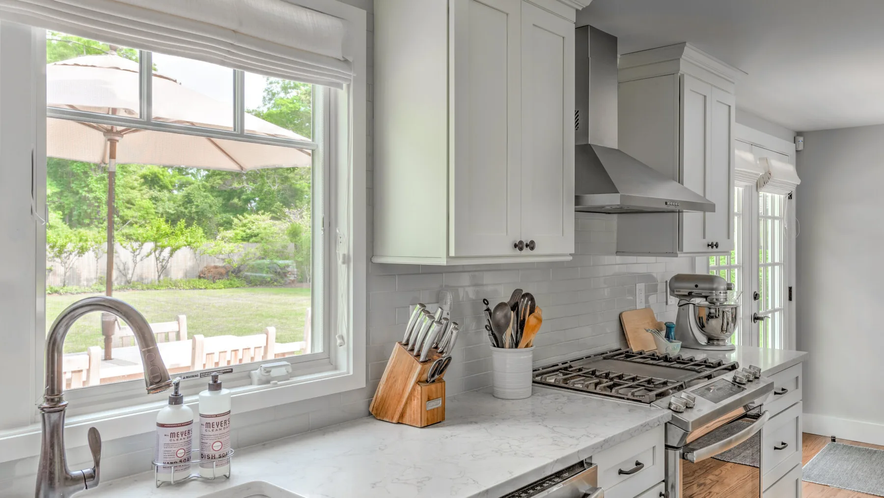 A bright kitchen with white cabinets, a cooktop, and a window overlooking greenery.