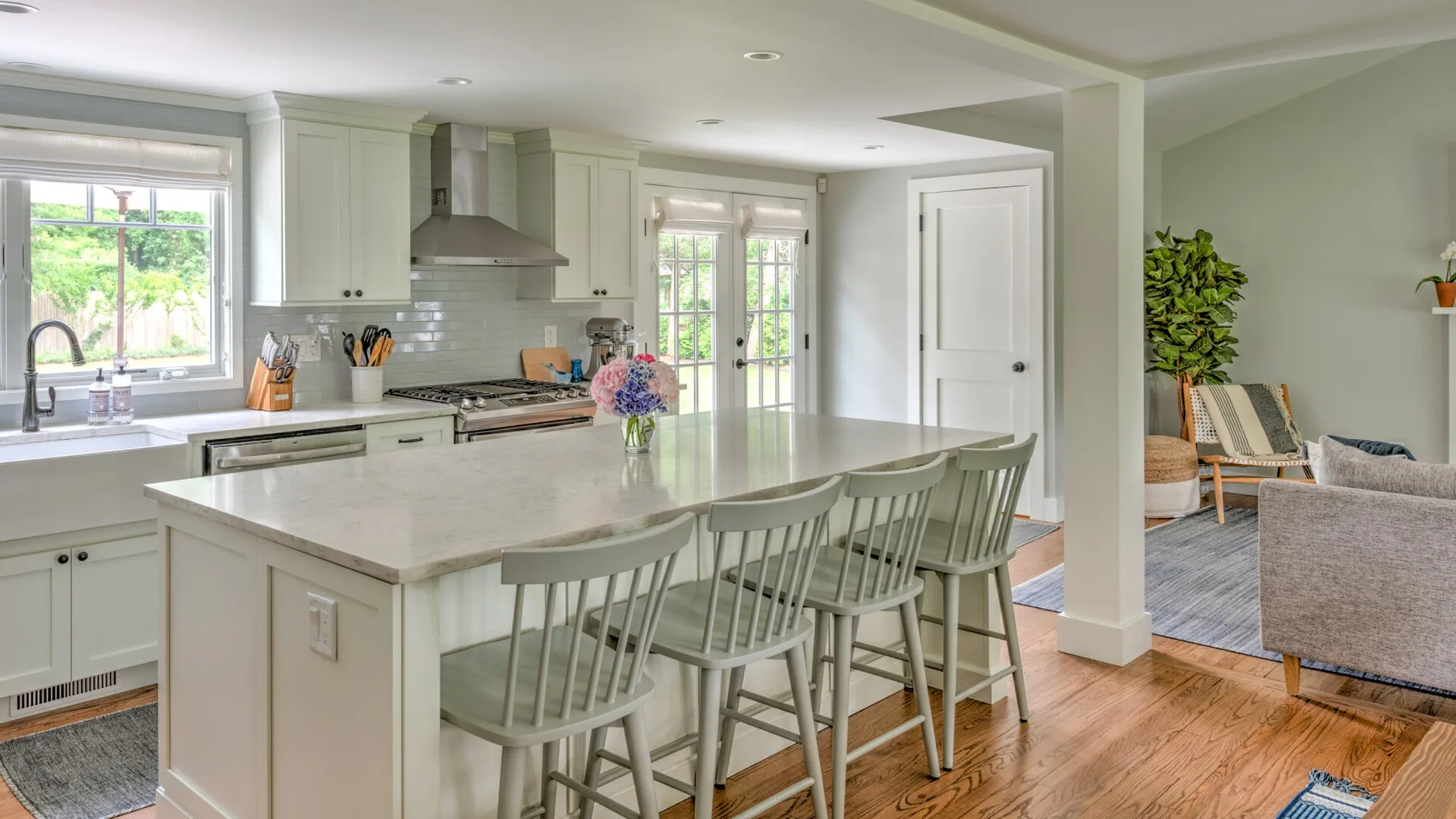 A bright kitchen with a large island and seating, opening onto a living area.