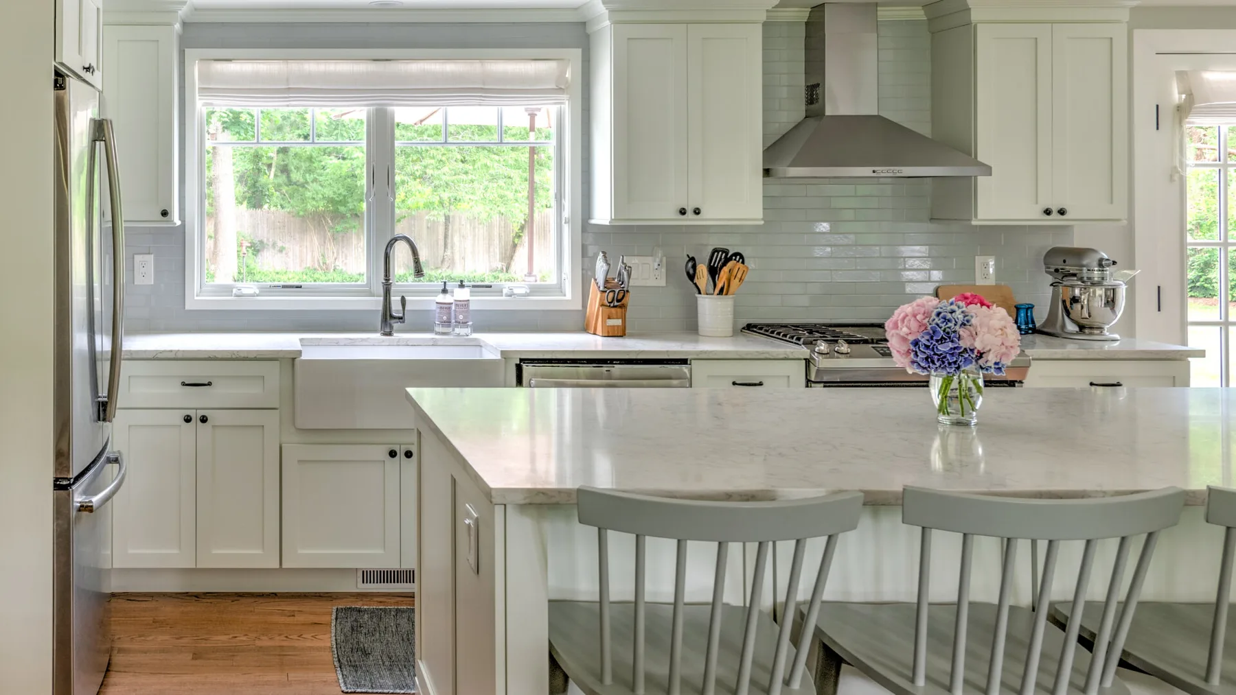 A bright kitchen with white cabinets, a central island, and windows overlooking greenery.