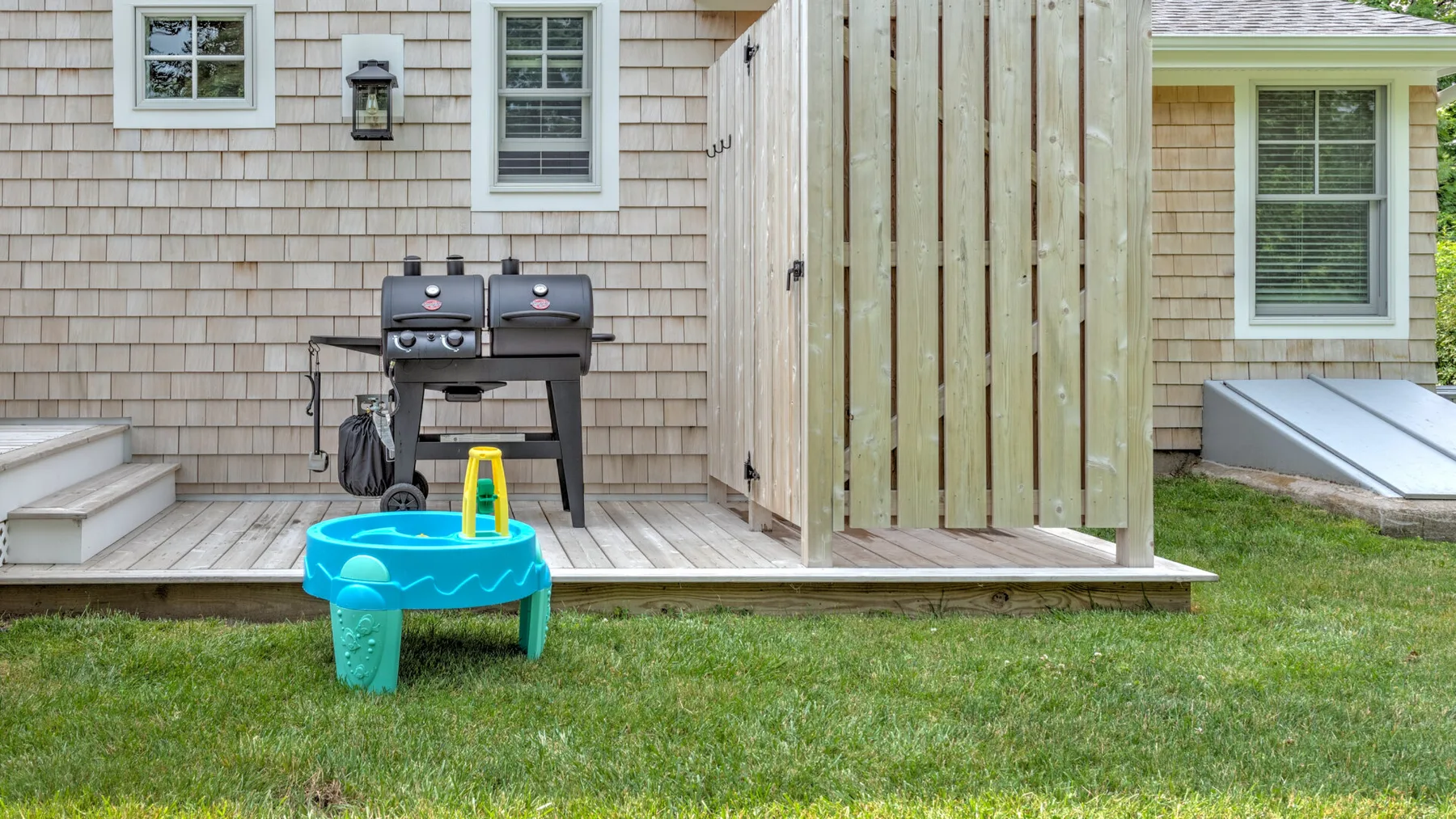 An outdoor patio with a grill and a small blue water table on the lawn.