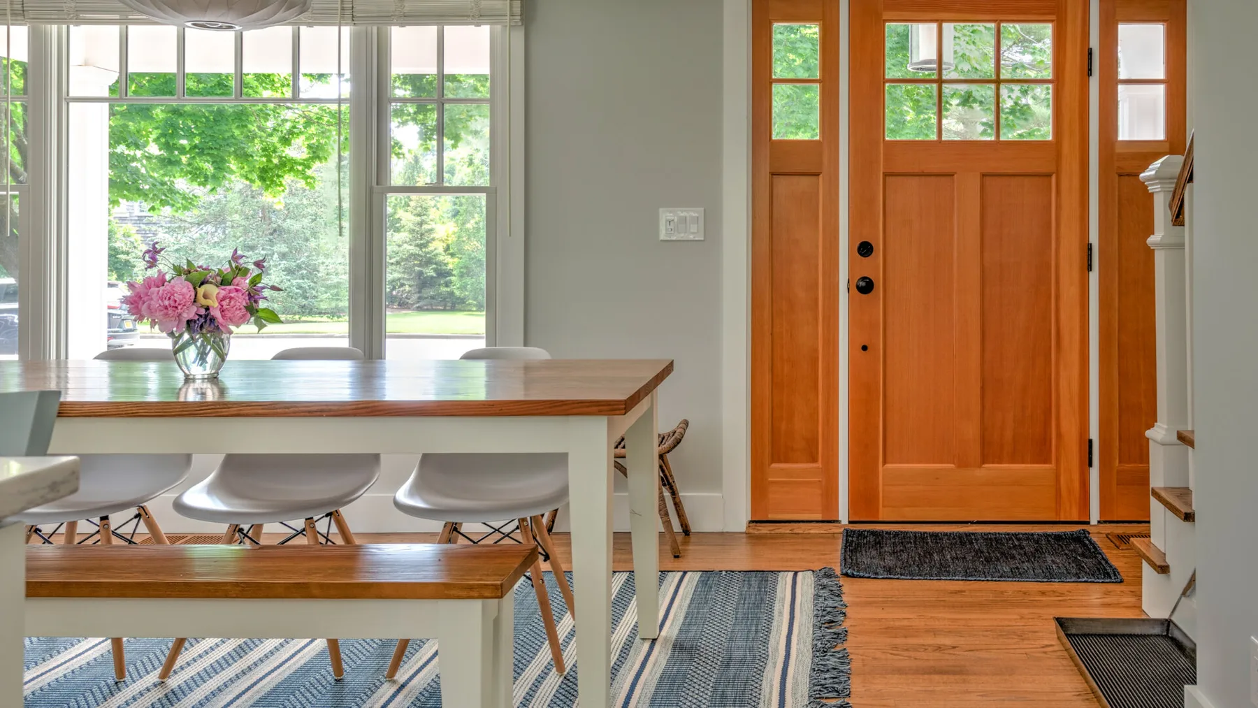 A bright dining area with a long table beside a wooden entry door.